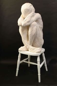 a white sculpture sitting on top of a chair with it's arms wrapped around the back