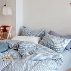 an unmade bed with blue and white checkered comforter, pillows and lamps