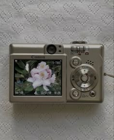 a digital camera sitting on top of a white cloth covered tablecloth next to a flower