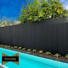 an empty swimming pool next to a tall black fence with trees and bushes on the other side