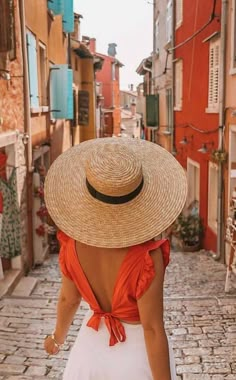 a woman wearing a straw hat walks down an alleyway between buildings in venice, italy