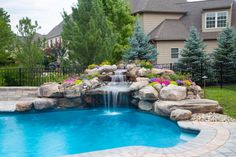 a backyard pool with waterfall and landscaping around it