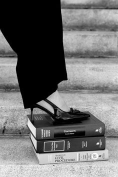 black and white photograph of woman's feet on books in front of stairs with steps