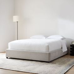 a white bed sitting on top of a wooden floor next to a lamp and rug