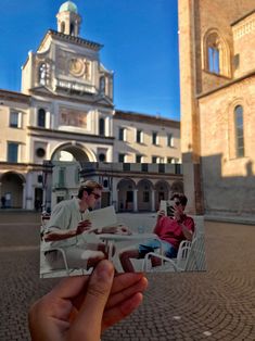 a person holding up an old photo in front of a building with a clock tower