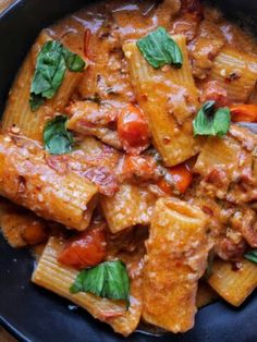 pasta with meat and tomato sauce in a black bowl on a wooden table, ready to be eaten