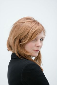 a woman with red hair is wearing a black jacket and looking off into the distance