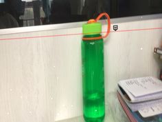 a green water bottle sitting on top of a counter next to a stack of books