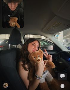 a woman sitting in the back seat of a car holding a teddy bear and making peace sign