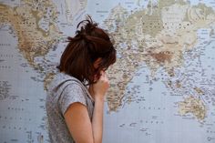 a woman standing in front of a world map holding her hand to her face and looking down