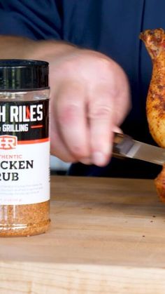 a person cutting up some food on top of a wooden table next to a jar of chicken rub