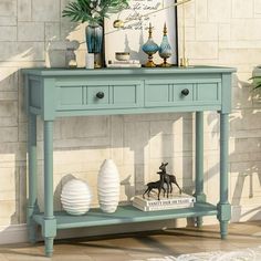 a blue console table with two white vases on it and a framed print above