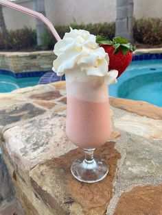 a strawberry milkshake sitting on top of a rock next to a swimming pool