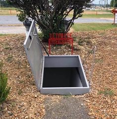 an open metal box sitting in the ground next to a tree and some signs on it