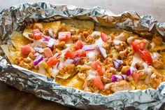 an enchilada dish with meat, onions and tomatoes in foil on a wooden table