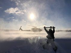 a helicopter is flying low to the ground as a man holds his skis in front of him