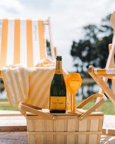 a bottle of champagne sitting on top of a wooden basket next to a beach chair