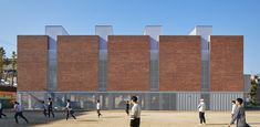 several people are walking around in front of a building with tall brick walls and windows