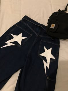 a pair of jeans with white stars painted on them and a black bag sitting next to it