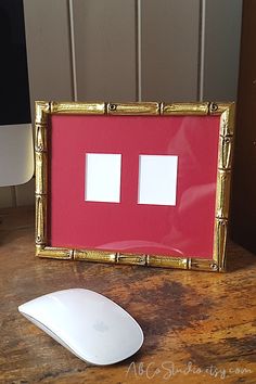 a computer mouse sitting on top of a wooden desk next to a red framed photo