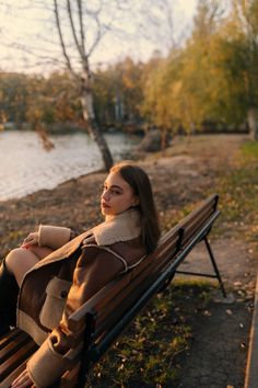 a woman is sitting on a bench by the water and looking off into the distance