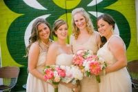 four bridesmaids pose for a photo in front of a green wall with white and pink flowers