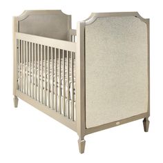 a baby crib with white linens on the sides and wood trimmings