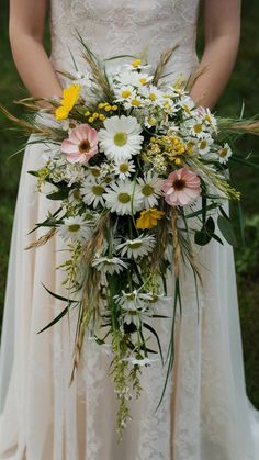 a bride holding a bouquet of white and yellow flowers on her wedding day in the grass