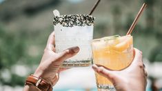 two people holding up glasses with drinks in them