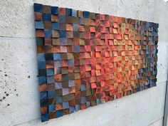 a wooden wall hanging on the side of a building with different colored wood pieces in it