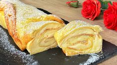 a pastry with powdered sugar is on a black plate next to flowers and red roses