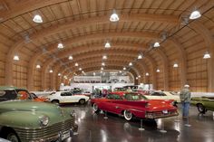 several classic cars are on display in a large room with wood paneling and ceiling lights