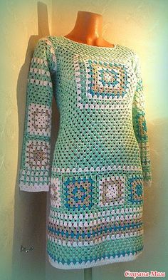 a green and white crocheted sweater on a mannequin head stand with a light behind it