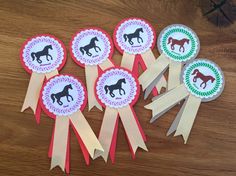 five ribbons with horses on them sitting on a wooden table next to other ribbon decorations