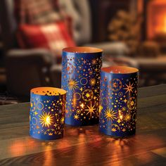 three blue candle holders with gold stars on them sitting on a table in front of a fire place