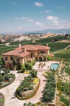 an aerial view of a large home surrounded by rolling hills and greenery with a pool in the foreground