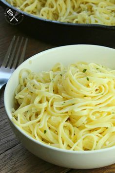 a white bowl filled with pasta on top of a wooden table next to a skillet