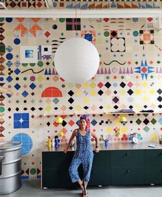 a woman is standing in front of a colorful wallpapered kitchen with a large white ball hanging from the ceiling