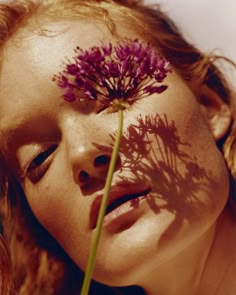 a woman with her eyes closed is holding a dandelion in front of her face