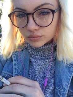 a blonde woman with glasses and headphones is looking at her cell phone while wearing earbuds