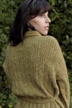 a woman standing in front of some bushes wearing a green cardigan sweater and black pants