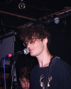 a young man standing in front of a microphone on top of a stage with another person behind him