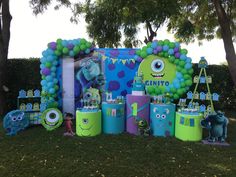 an outdoor birthday party with balloons and decorations on the grass, including monster characters in front of a giant balloon arch