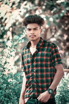 a young man standing in front of some bushes wearing a green and red checkered shirt