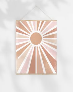 a pink and gold sunburst print hanging on a wall with a white background