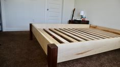 a wooden bed frame in a bedroom with carpeted flooring and white walls behind it