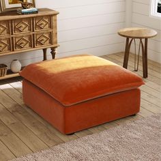 an orange ottoman sitting on top of a wooden floor next to a dresser and table