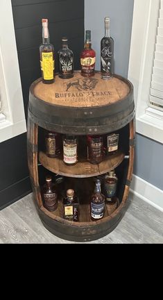 a barrel table with liquor bottles on it and two shelves in the middle that hold whiskey