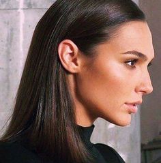 a woman with long hair wearing a black shirt and looking off to the side while standing in front of a wall