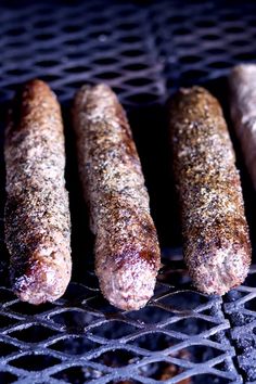 four sausages are cooking on the grill with seasoning sprinkled over them